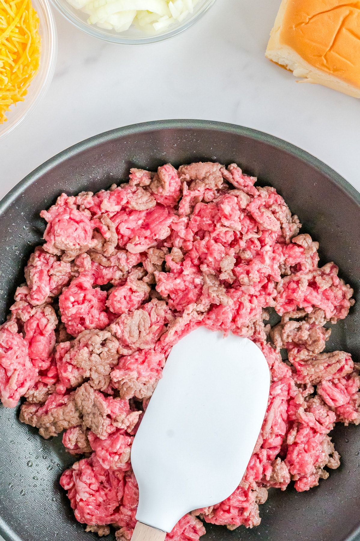 A frying pan with ground beef in the process of being cooked, with some pink and some brown.