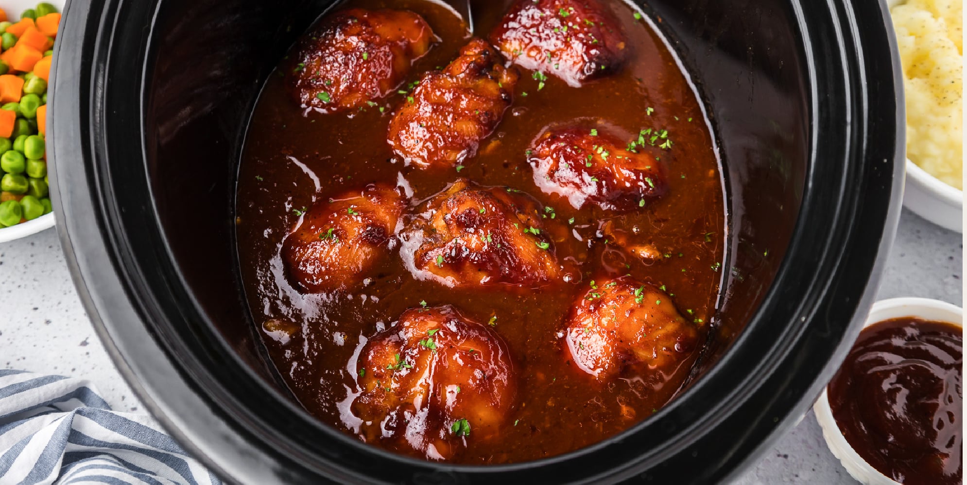 Wide view of cooked chicken thighs in bbq sauce in a crockpot.