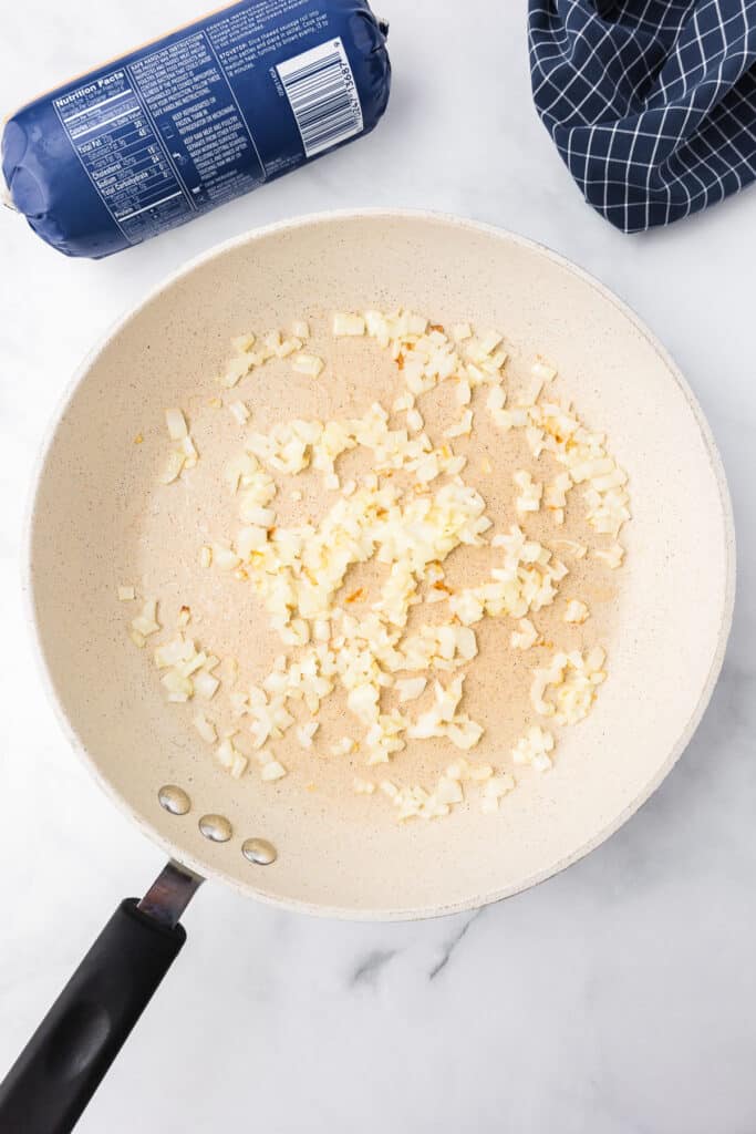 A frying pan with onions, a pack of sausage and a kitchen towel next to it.