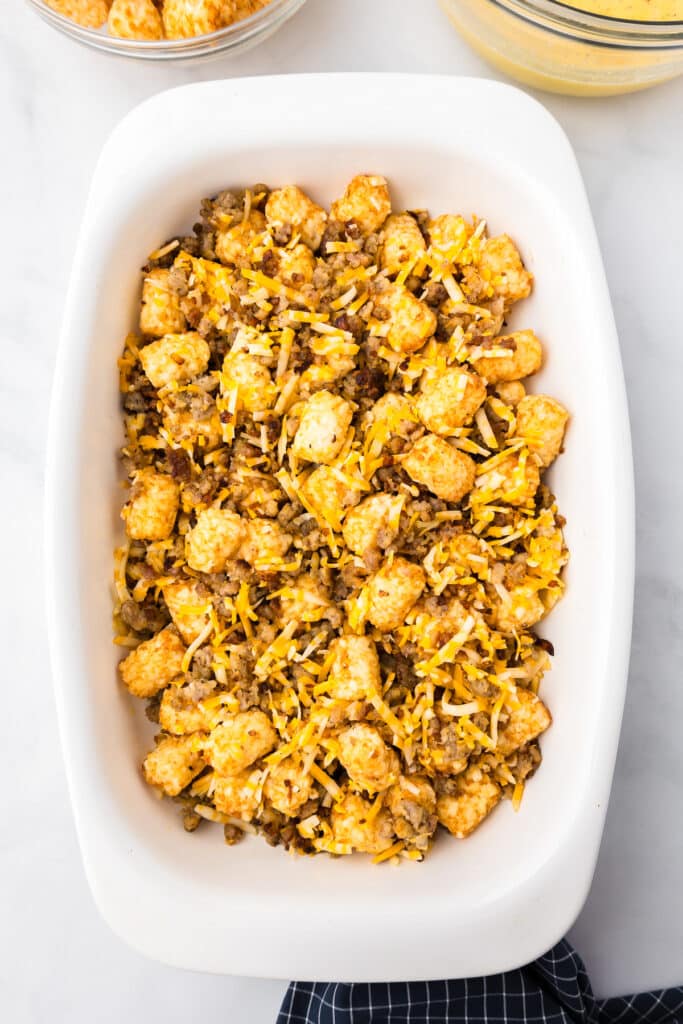 Tater tots, sausage and cheese mixed together in a casserole dish from above.