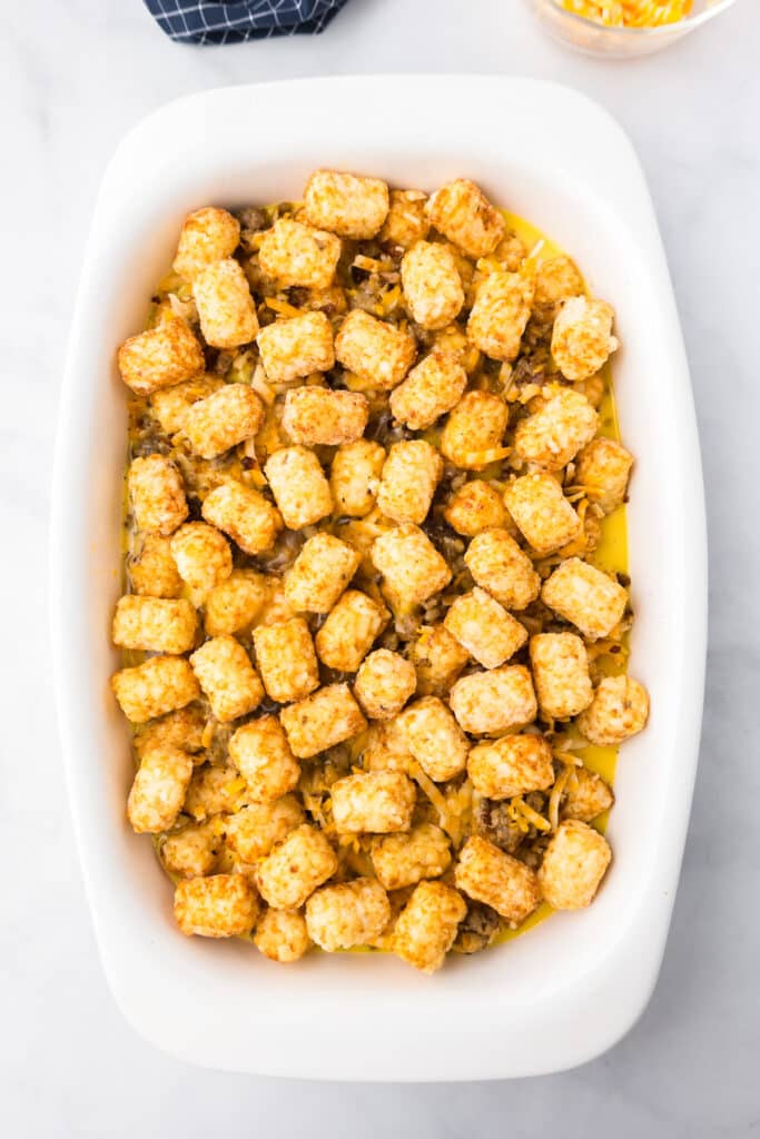 Tater tot casserole with frozen tater tots on top before baking.