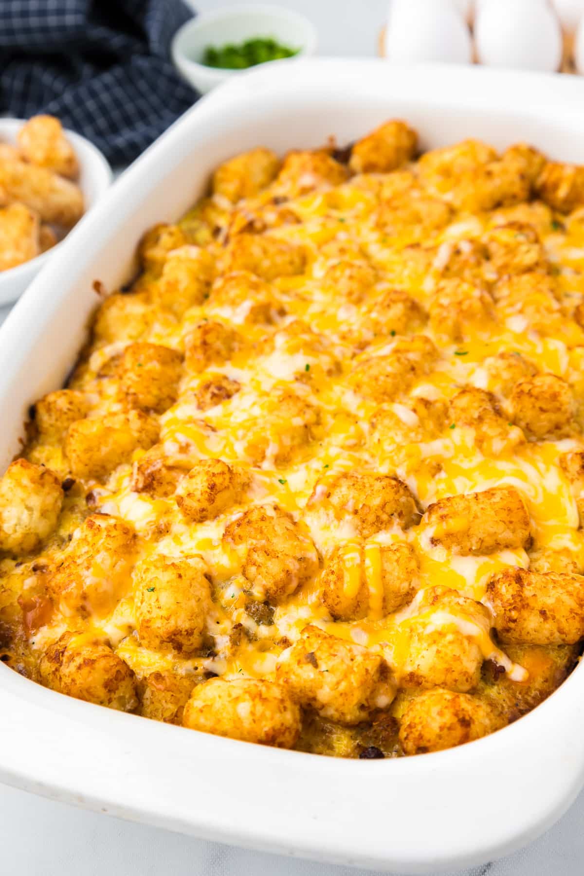 A white casserole dish with cheesy tater tot breakfast casserole from the side..
