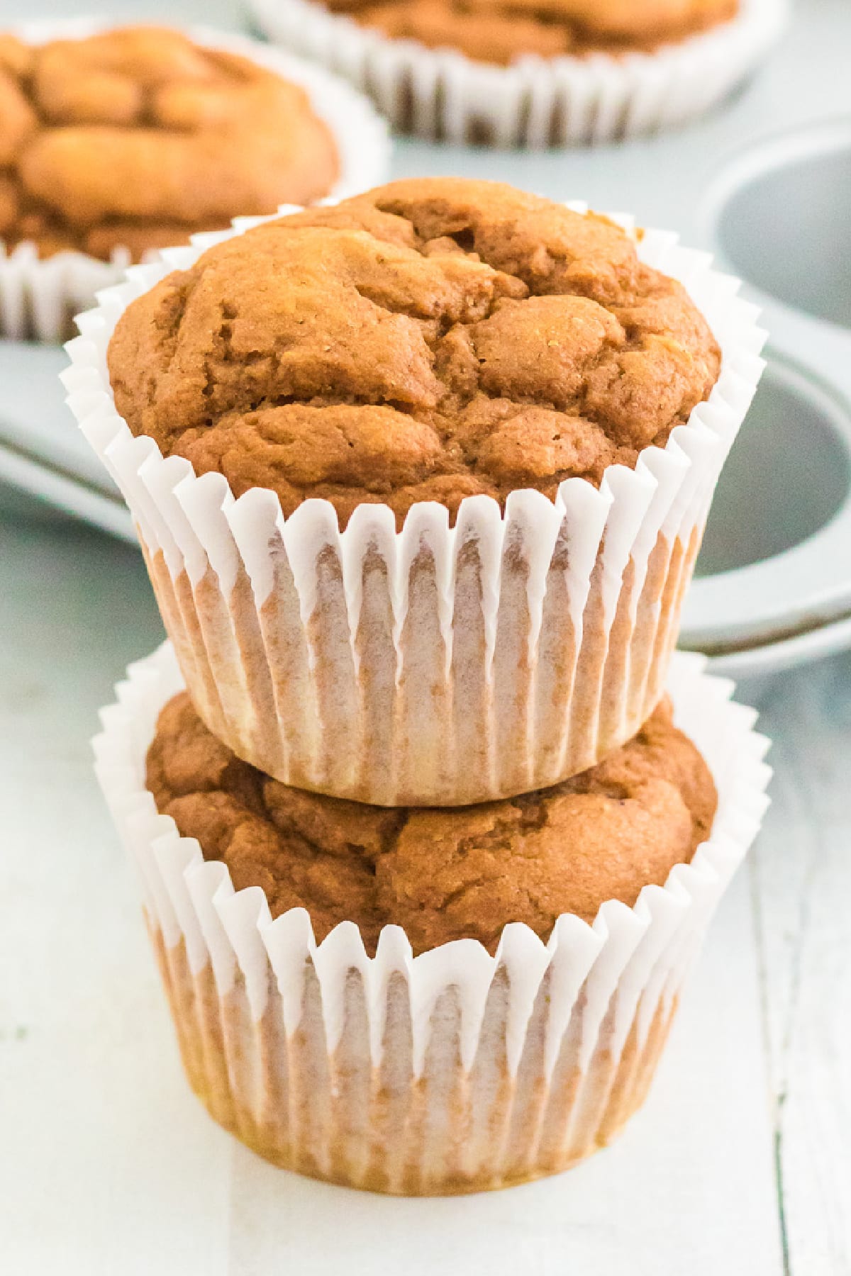 A stack of two pumpkin muffins with a muffin tin behind.