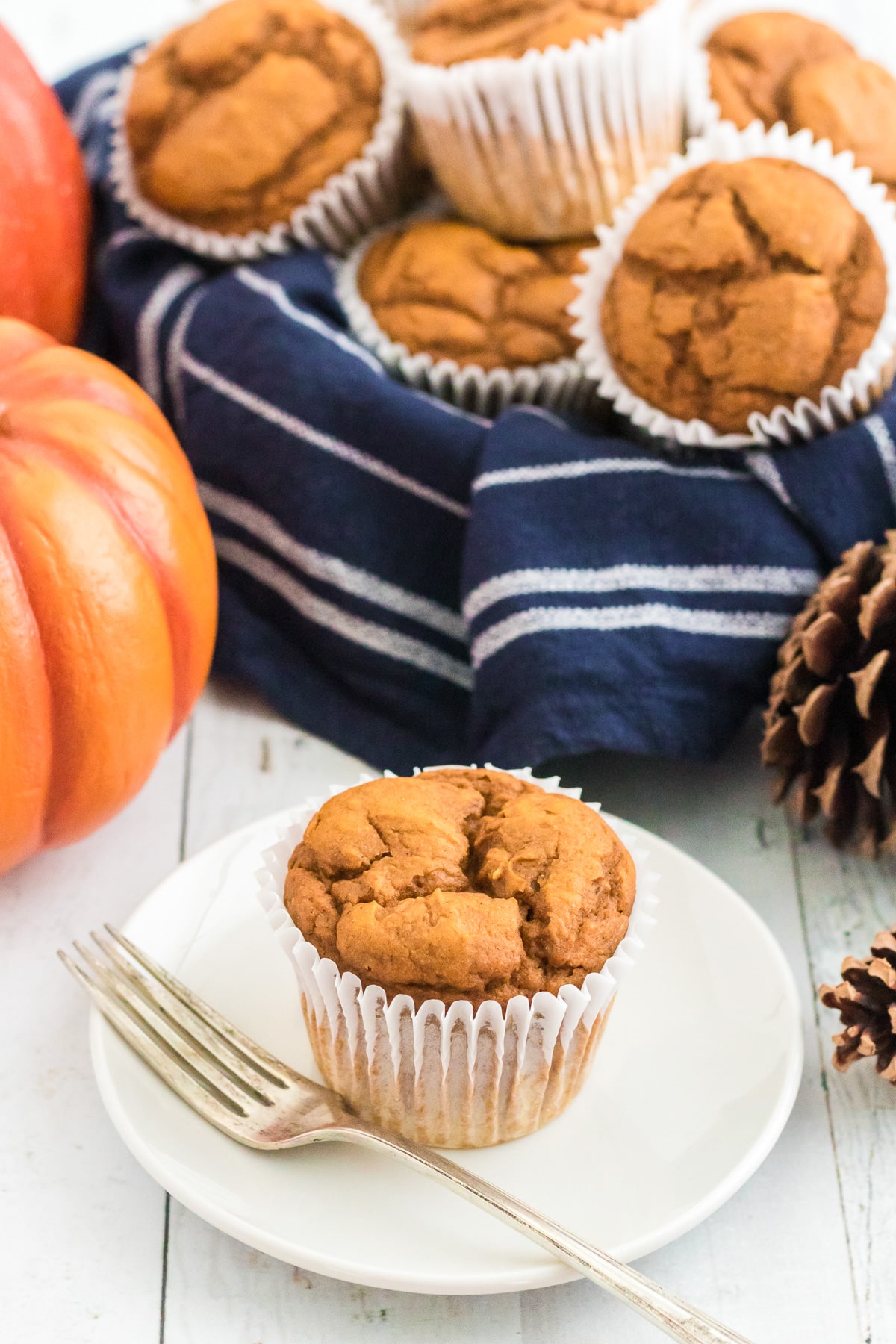Pumpkin muffin on a plate with a fork with a bowl full of pumpkin muffins in the background..