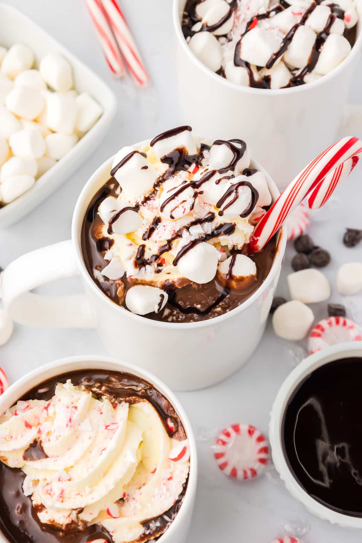 Three mugs of hot chocolate with candy canes, whipped cream and marshmallow toppings.