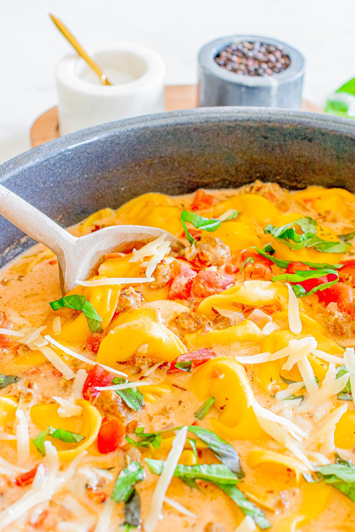 A pan with creamy sausage tortellini soup with a wooden spoon scooping a spoonful.