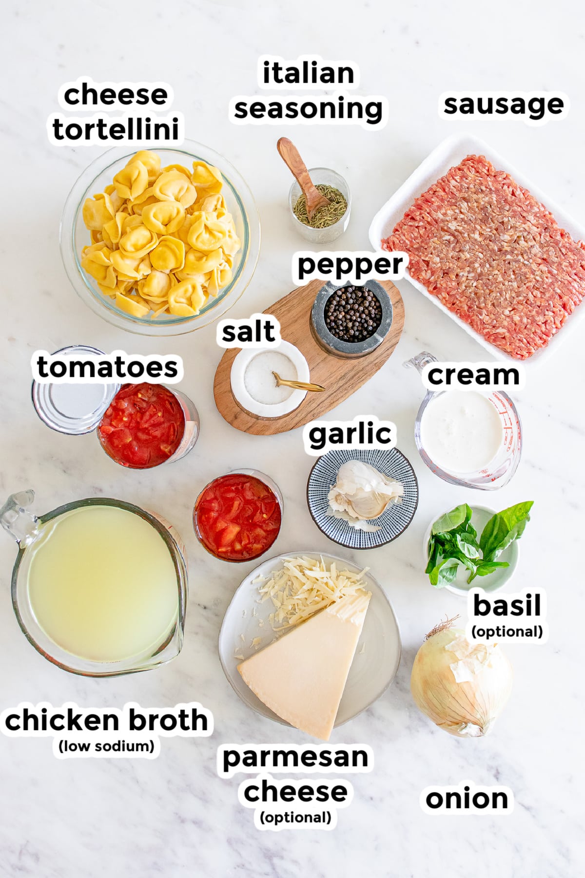 Ingredients for creamy sausage tortellini soup in bowls on a counter from above with title text labels.