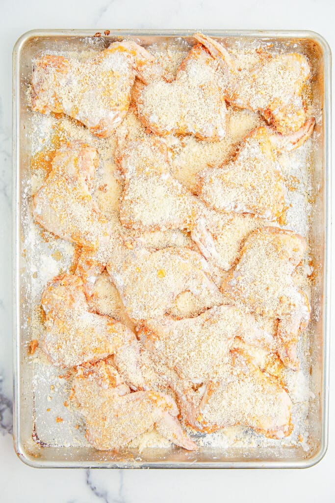 Chicken wings on a baking pan covered in cornstarch and parmesan cheese.