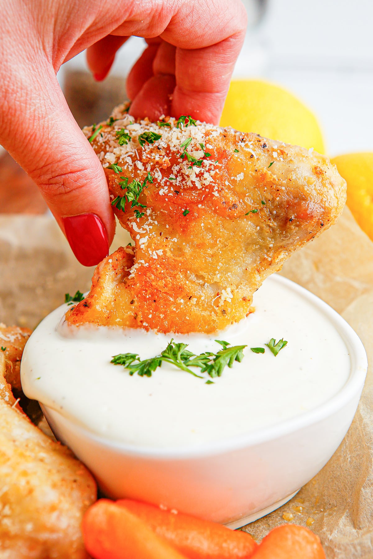 A person dipping a chicken wing into a bowl of dipping sauce.