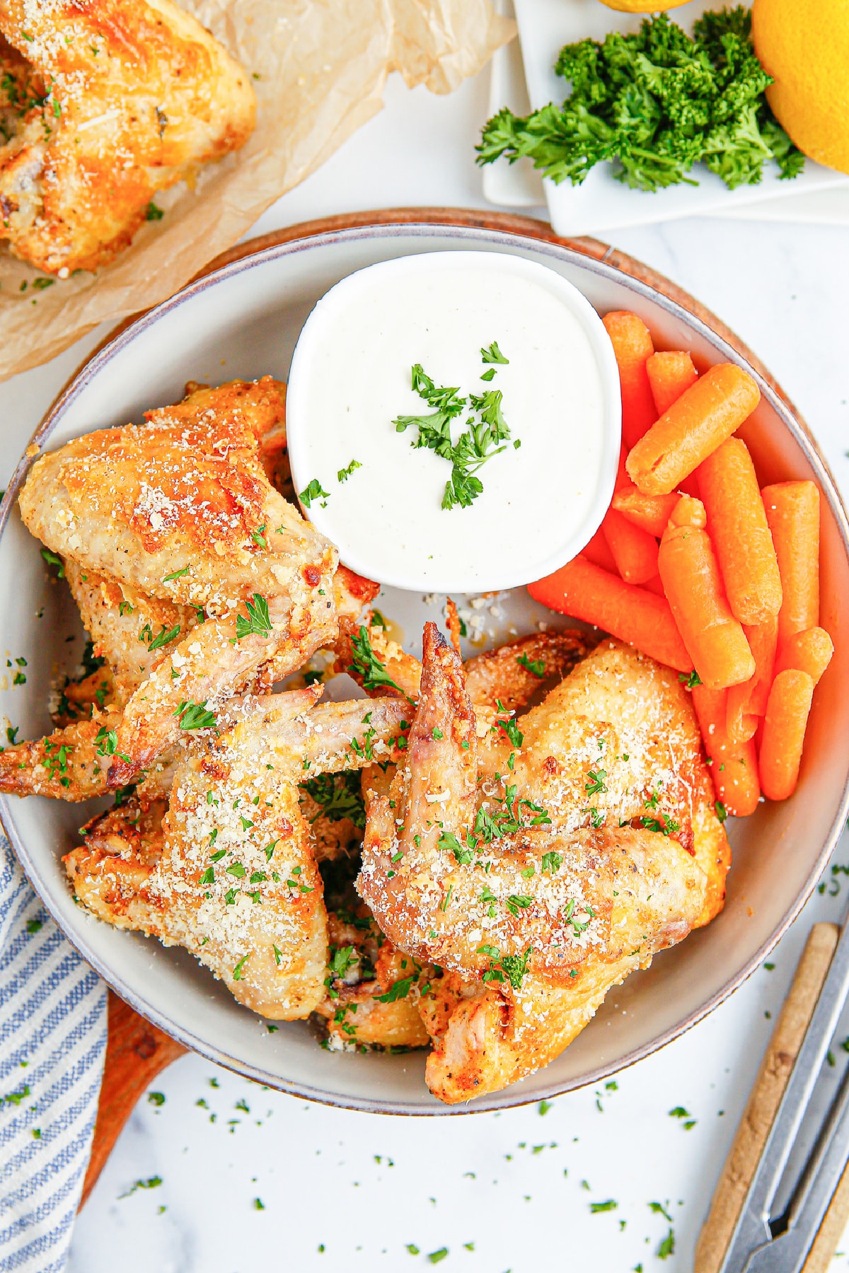 A bowl of chicken wings with carrots and dipping sauce with more chicken wings in a bowl on the side.