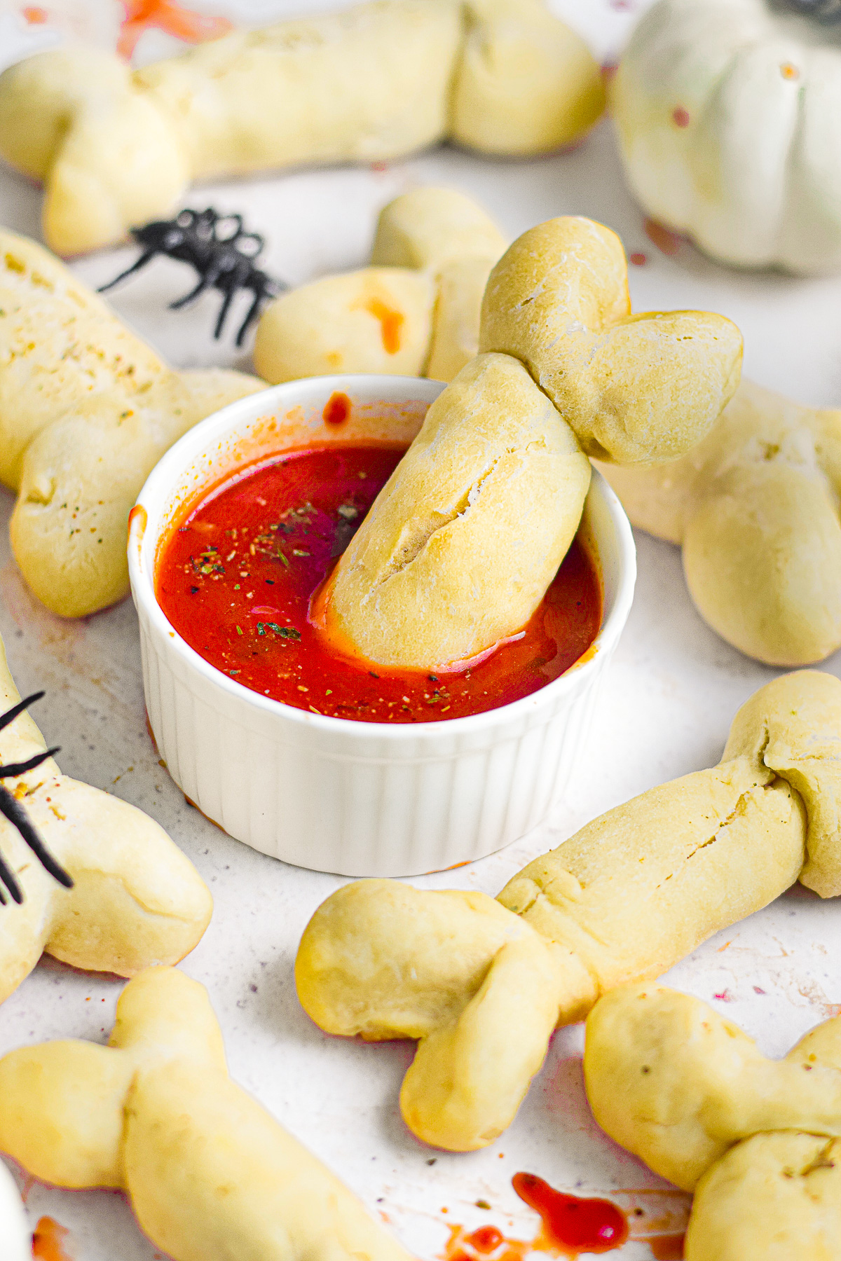A bone shaped breadstick being dipped in a bowl with a red marinara sauce with more breadsticks nearby on the platter.