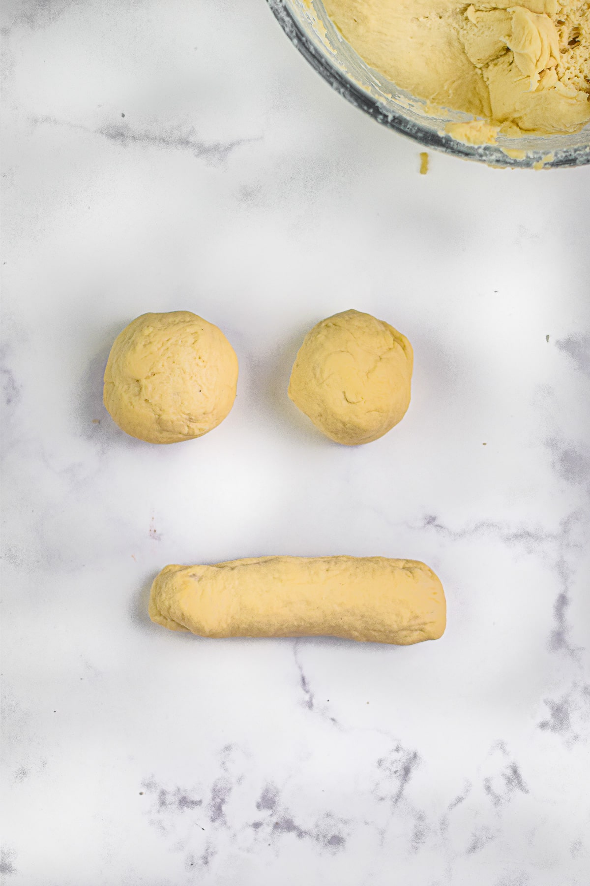 Two dough balls next to a long cylinder shaped piece of dough on a counter.