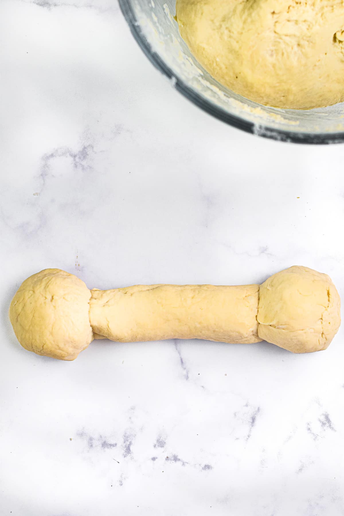 A long piece of dough with a dough ball on each end on a counter.