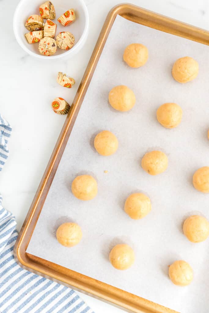 A baking sheet with rough truffle dough balls with peanut butter cups stuffed inside.