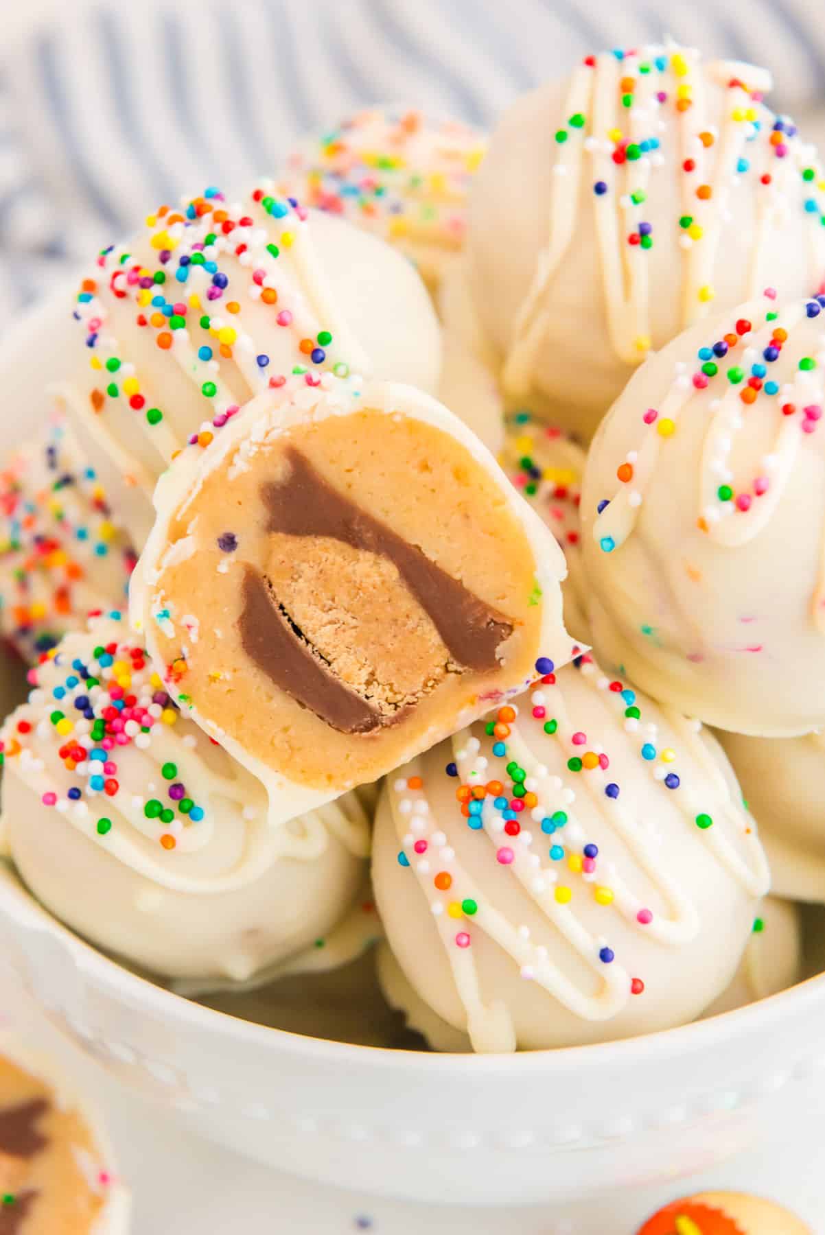 A bowl filled with white chocolate peanut butter balls with one showing the peanut butter cup inside and topped with sprinkles.