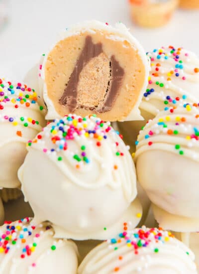 Peanut butter truffles with sprinkles on a plate with one cut so you can see a peanut butter cup on the inside.
