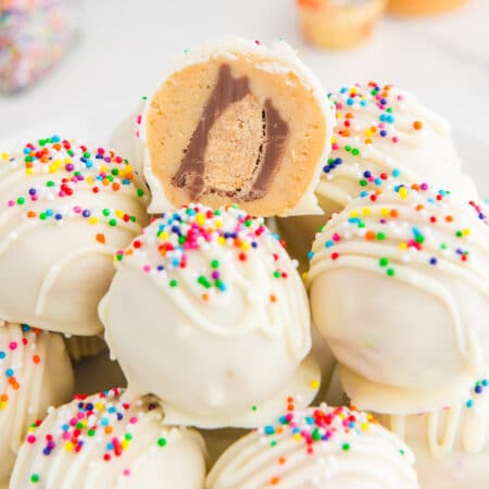 Peanut butter truffles with sprinkles on a plate with one cut so you can see a peanut butter cup on the inside.