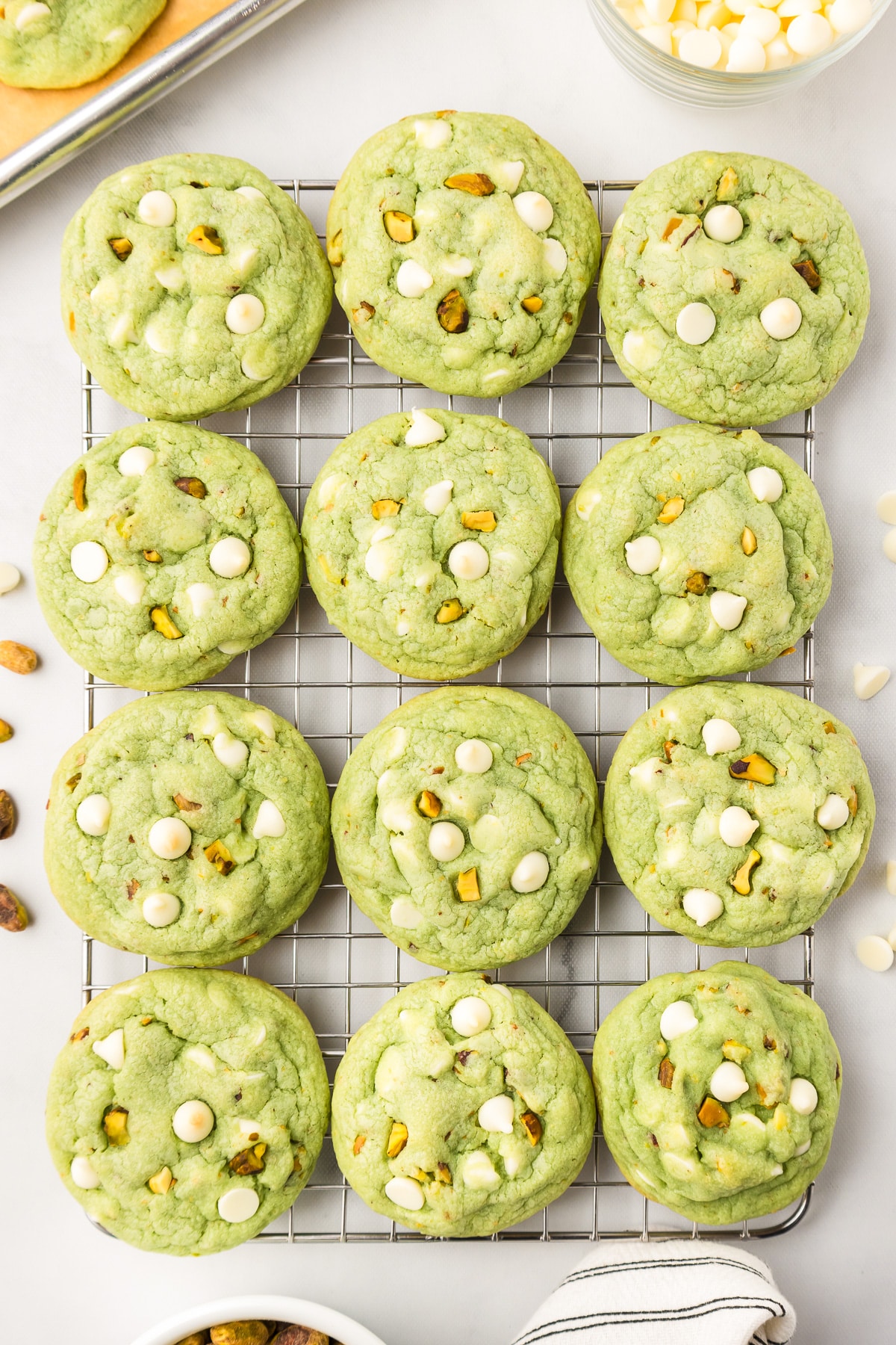 Green pistachio cookies with white chocolate chips on a cooling wire rack from above.