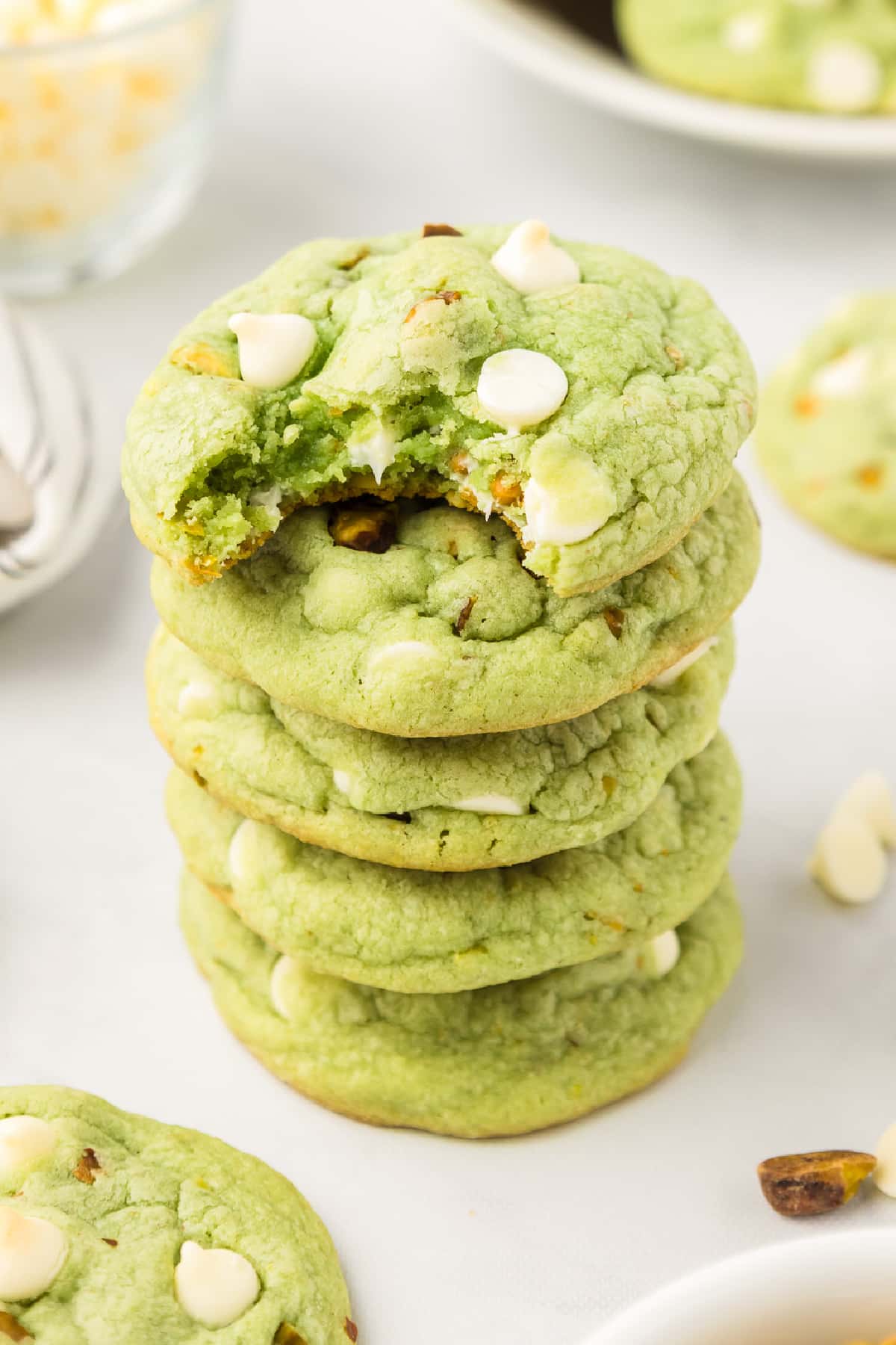 A stack of green pistachio pudding cookies with white chocolate chips with a bite taken out of the top cookie.