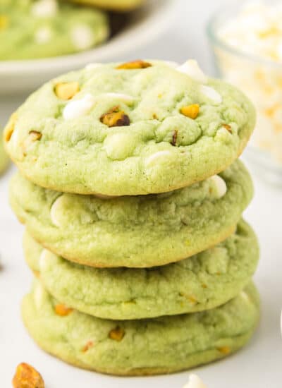 A stack of green pistachio pudding cookies four cookies tall with more cookies in the background.