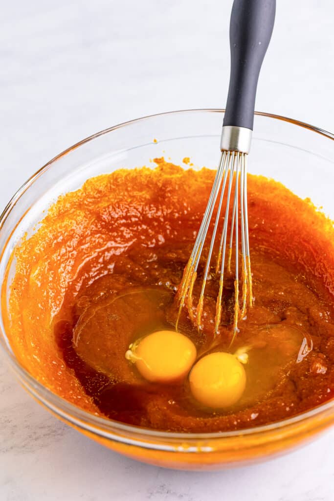 Two eggs being mixed into pumpkin batter mix in a bowl.