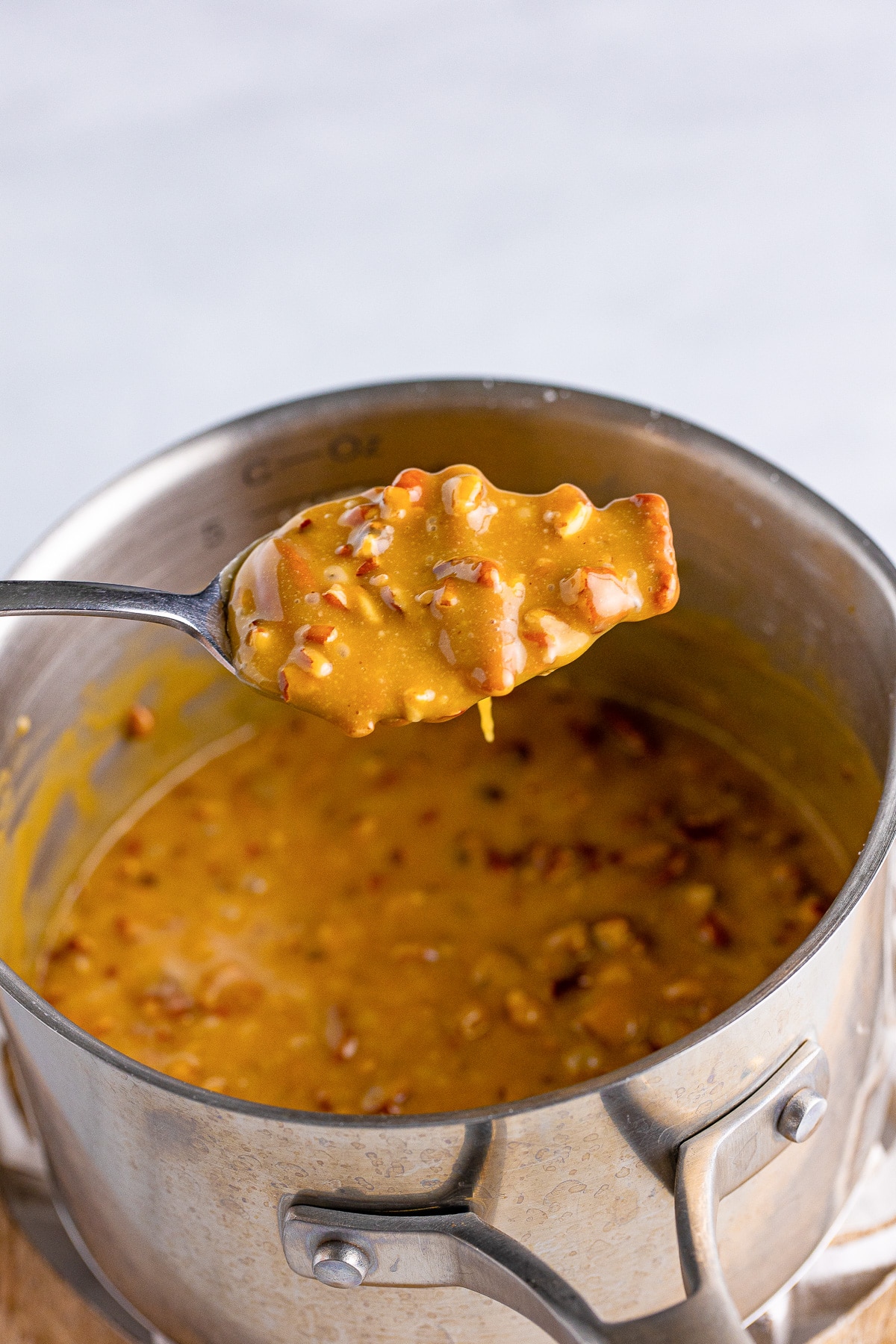 A spoon full of pumpkin praline mixture being lifted from a pot.