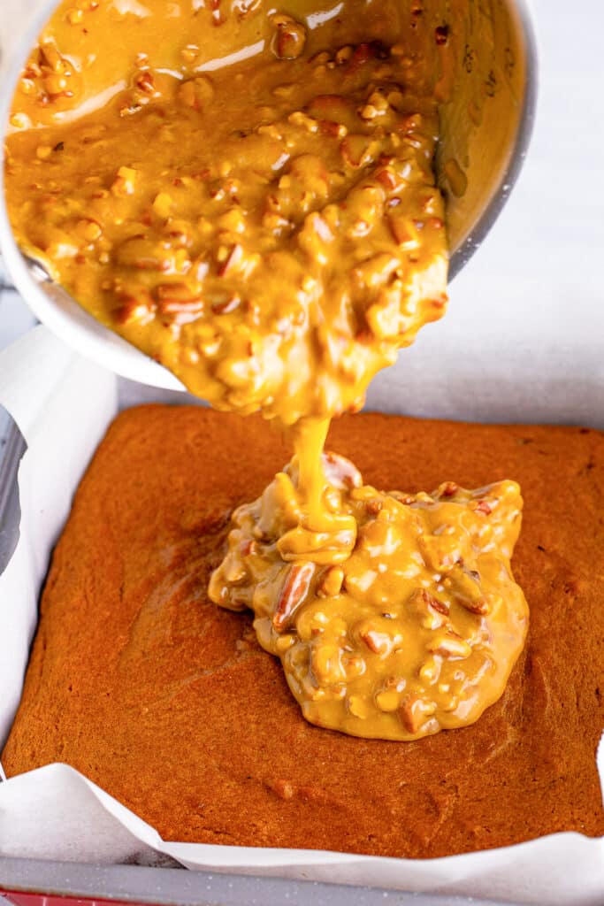 A pumpkin cake with praline pecan mixture being poured over top of the cake.