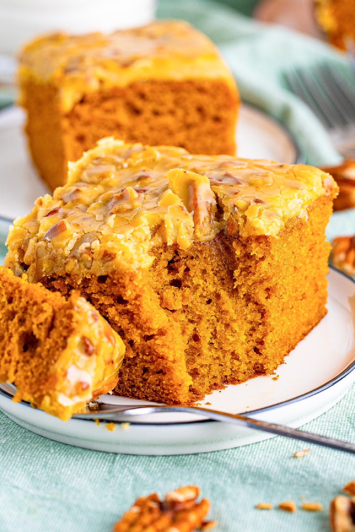 A slice of pumpkin cake topped with pecan praline topping on a plate with a fork missing a bite.