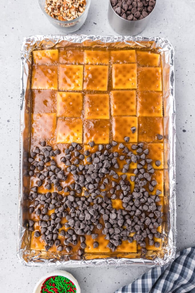 A baking pan filled with toffee covered saltines with half the pan also covered in chocolate chips.