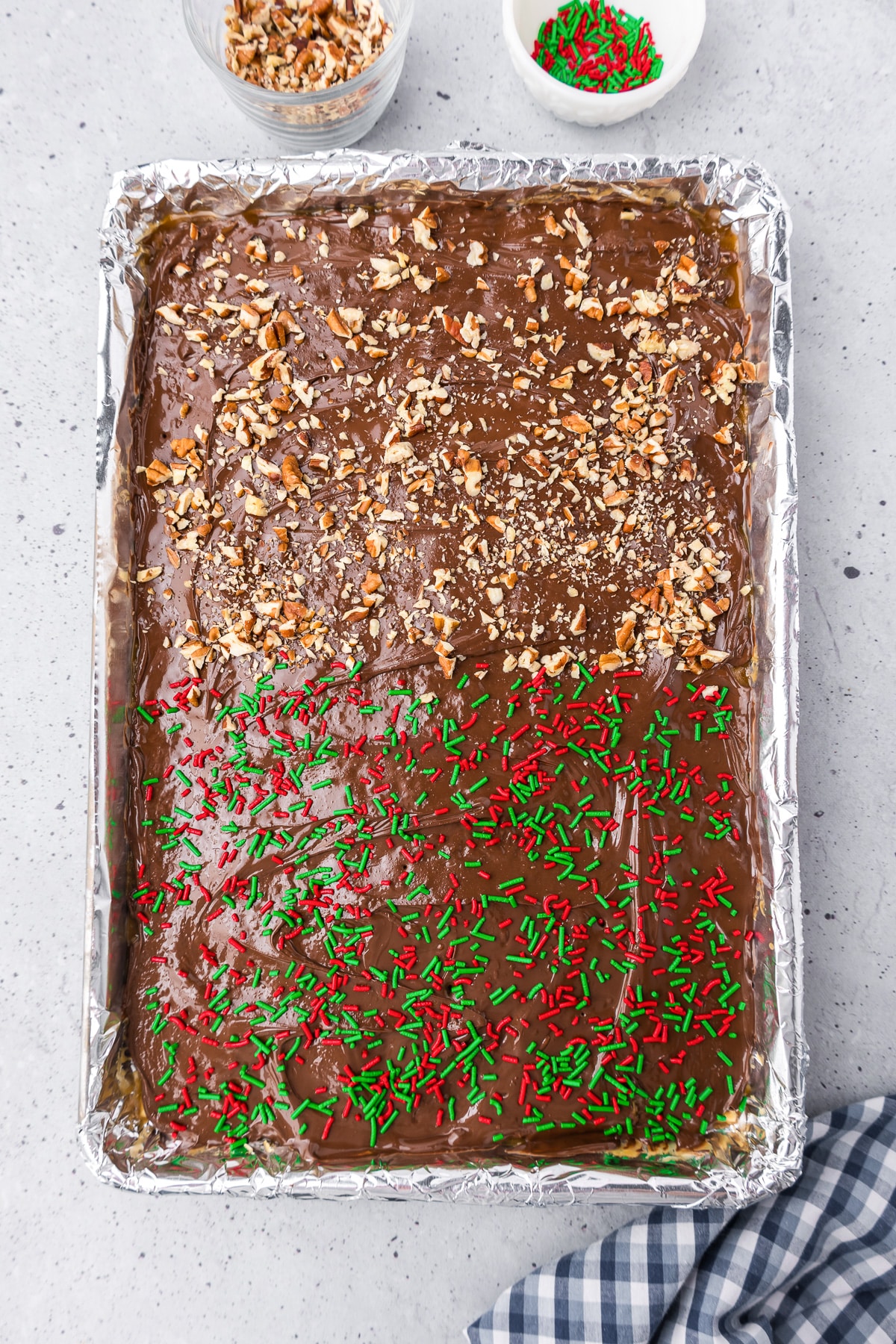 A pan of chocolate toffee half covered with sprinkles and half covered with pecans.