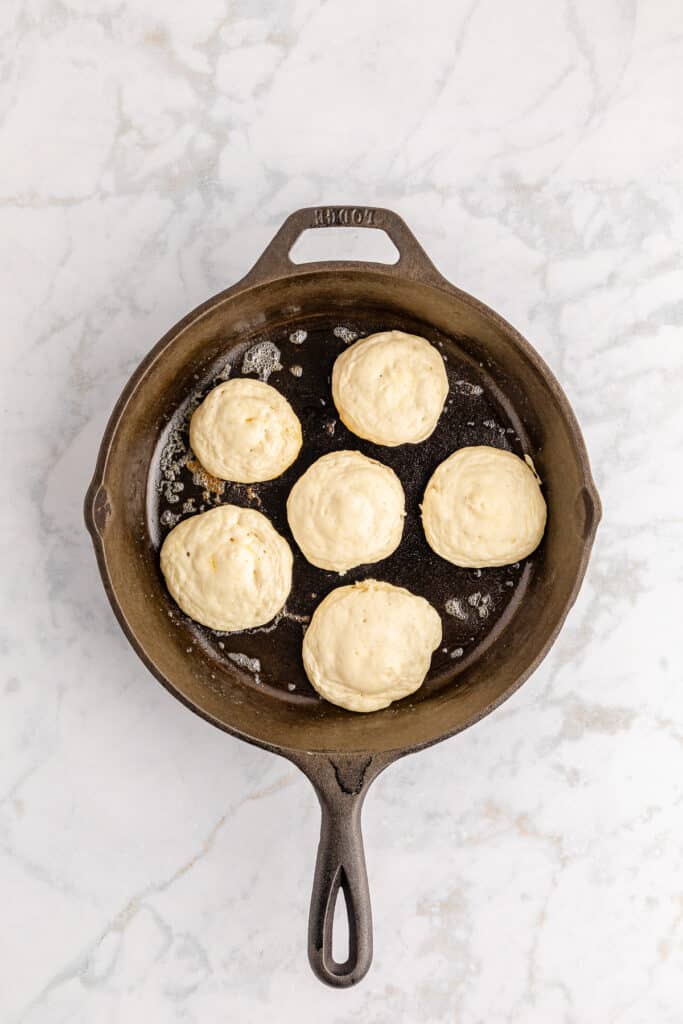 Silver dollar pancakes being cooked in a skillet overhead on a counter.