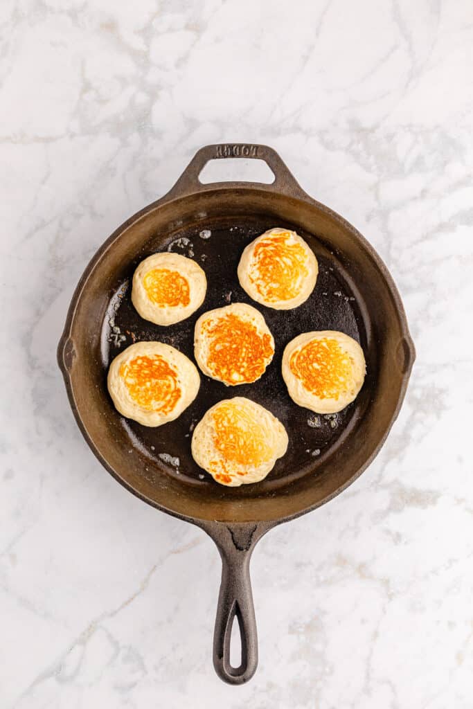 Silver dollar pancakes being cooked in a skillet after flipping now golden brown from overhead on a counter.