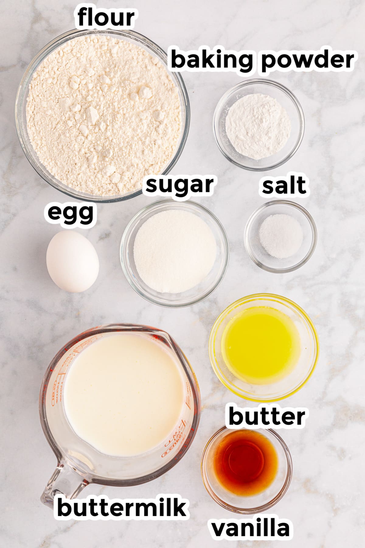 Ingredients for silver dollar pancakes on a counter in bowls from overhead with text labels.