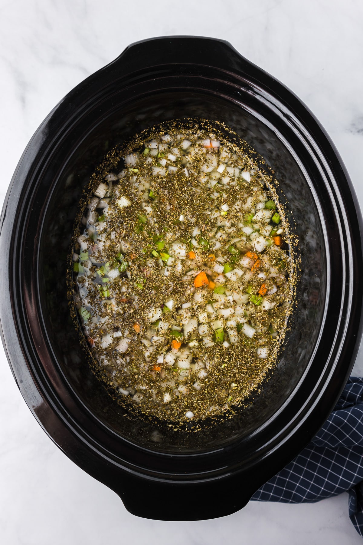 A crock pot filled with soup, vegetables and herbs for chicken gnocchi soup.