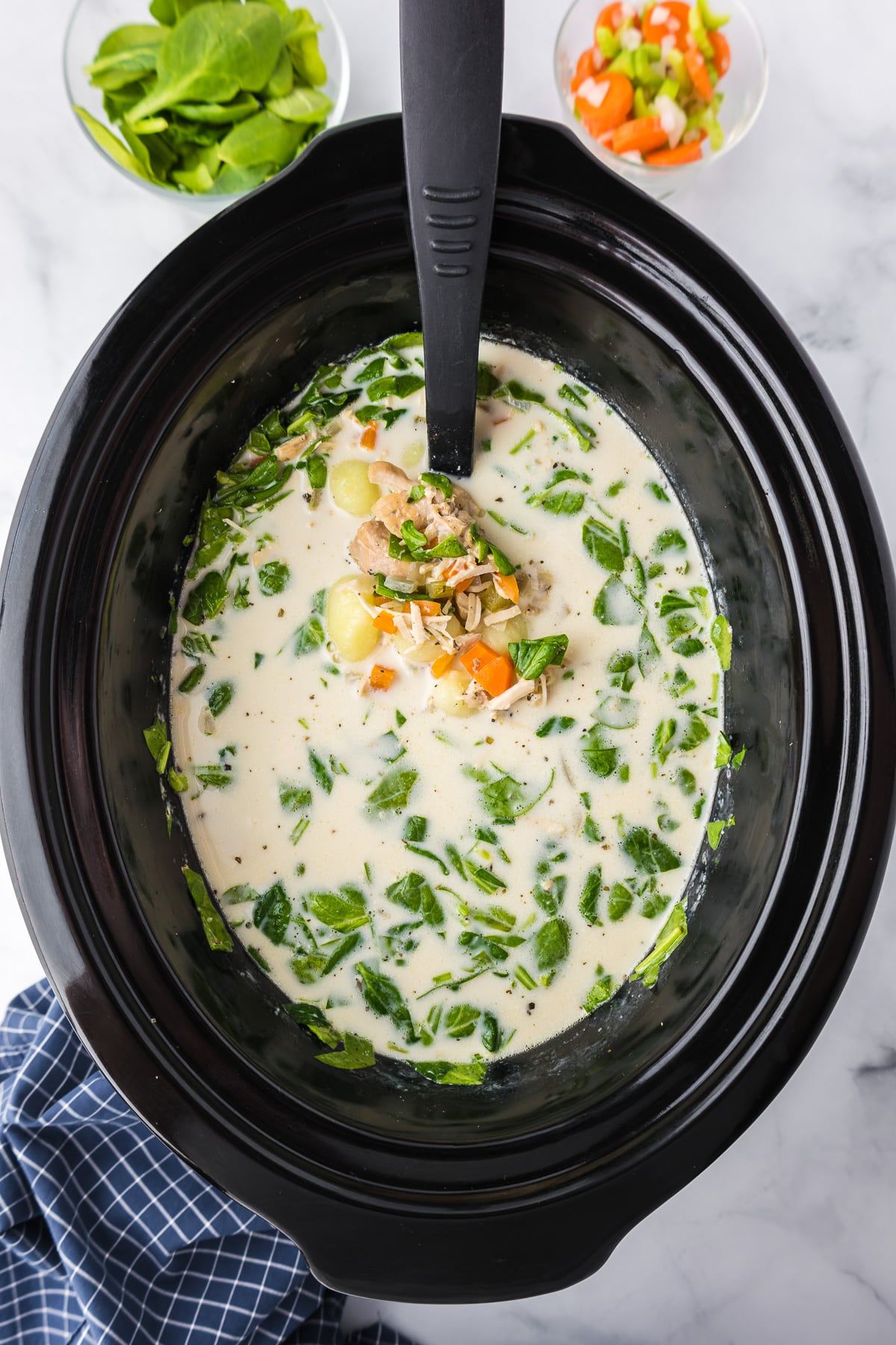 A slow cooker filled with a creamy gnocchi soup and spinach.