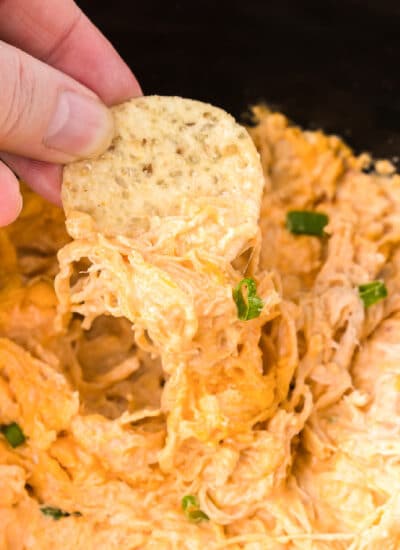 Fingers dipping a chip into buffalo chicken dip close up.