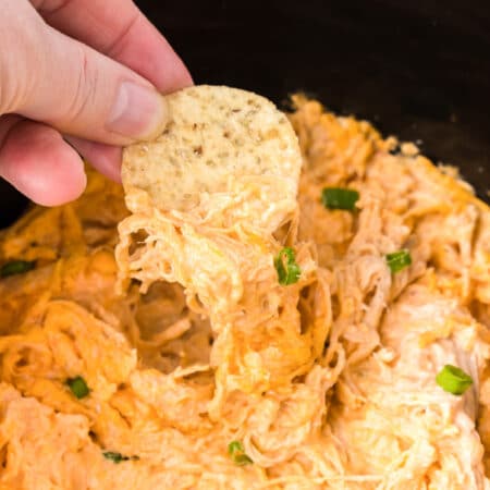 Fingers dipping a chip into buffalo chicken dip close up.