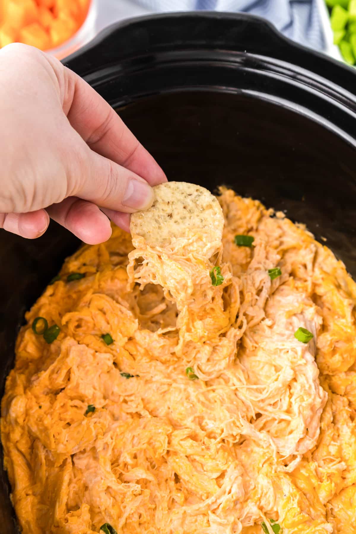 A person dipping a chip into a slow cooker bowl full of buffalo chicken dip.