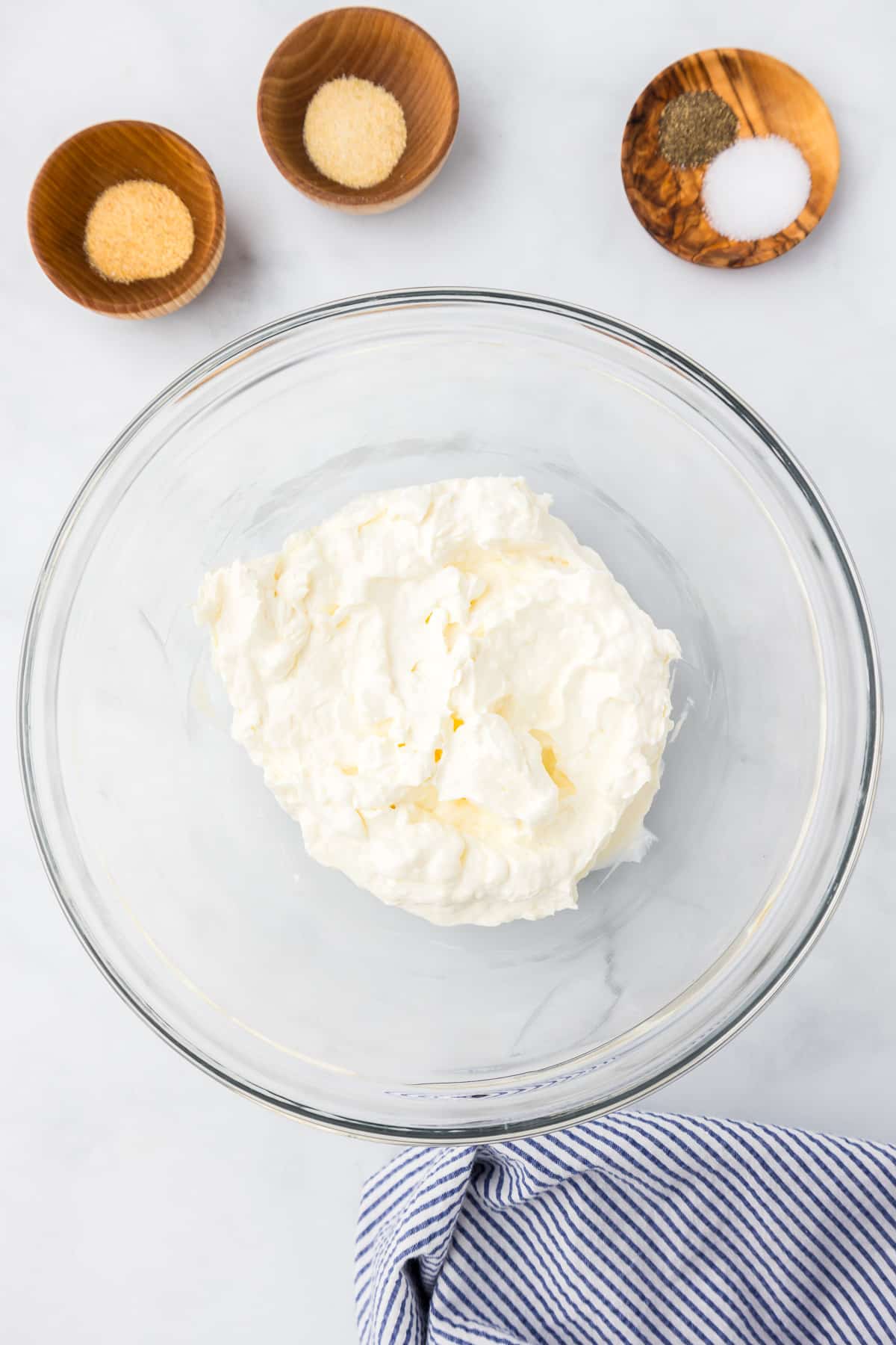 Sour cream and cream cheese mixed together in a glass bowl with spices in bowls nearby.