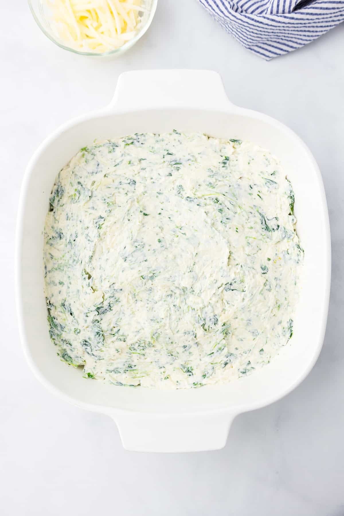 Cheesy spinach dip in a white square dish before baking.