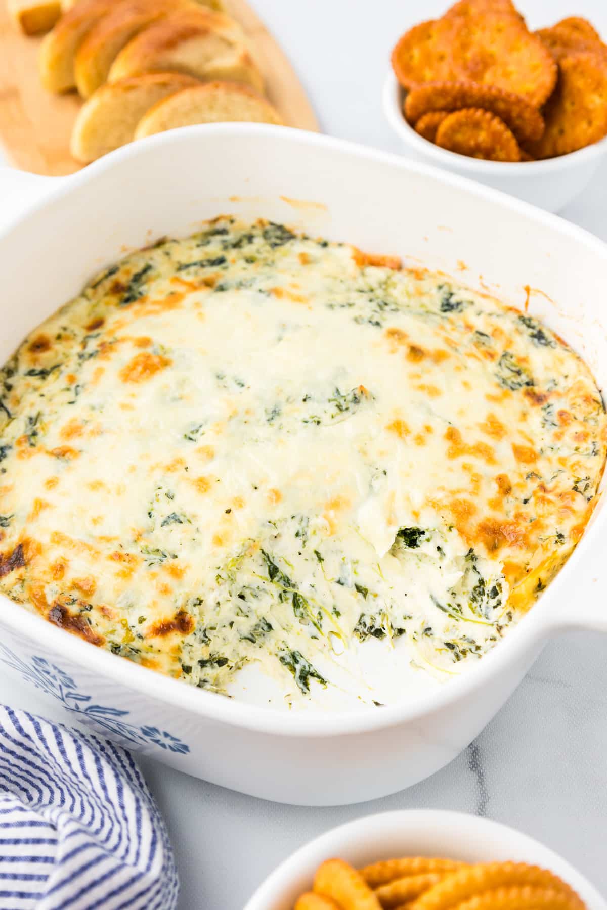Cheesy spinach dip in a white dish with a scoop missing.