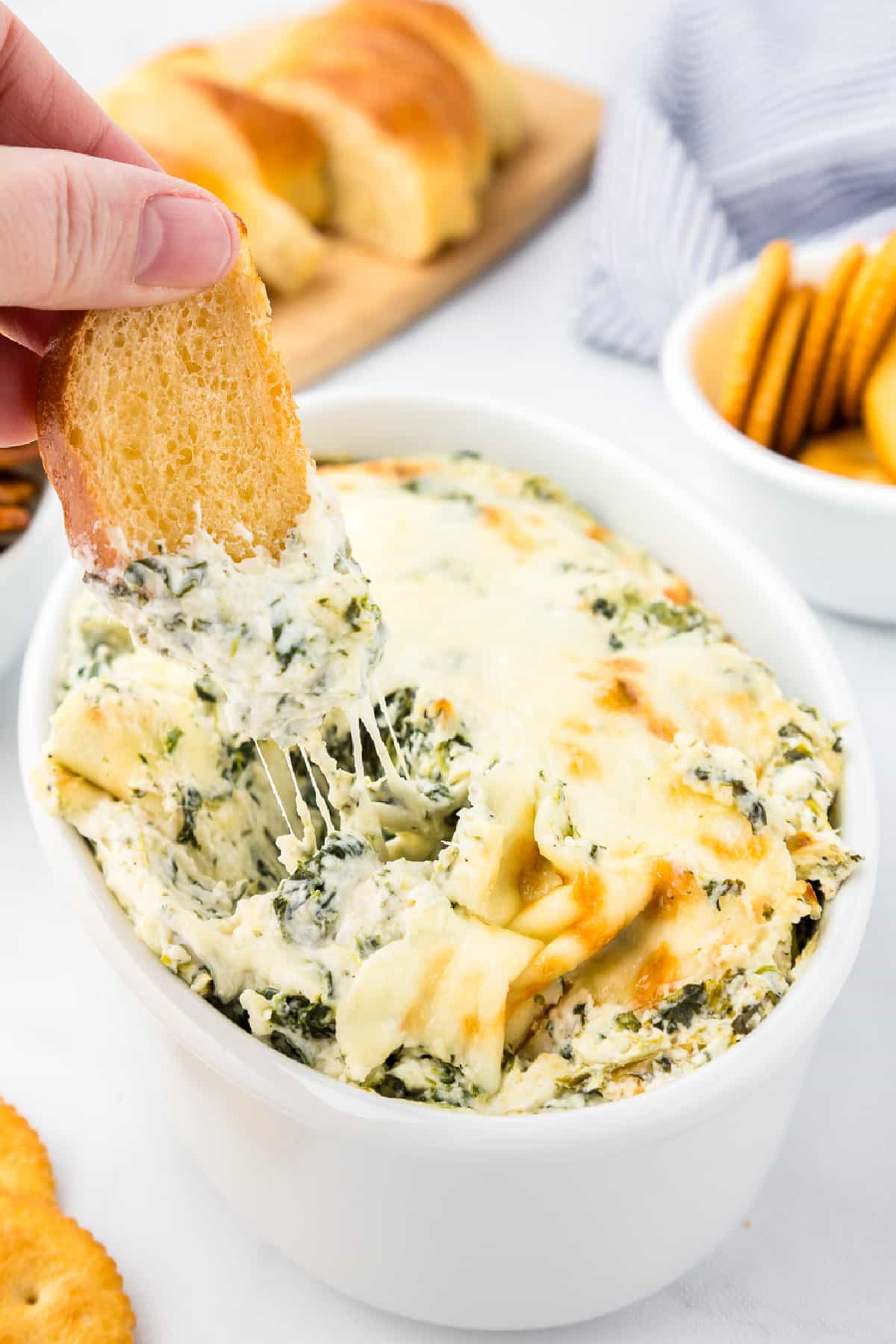 A person's hand dipping a piece of chewy bread into a bowl of cheesy spinach dip.