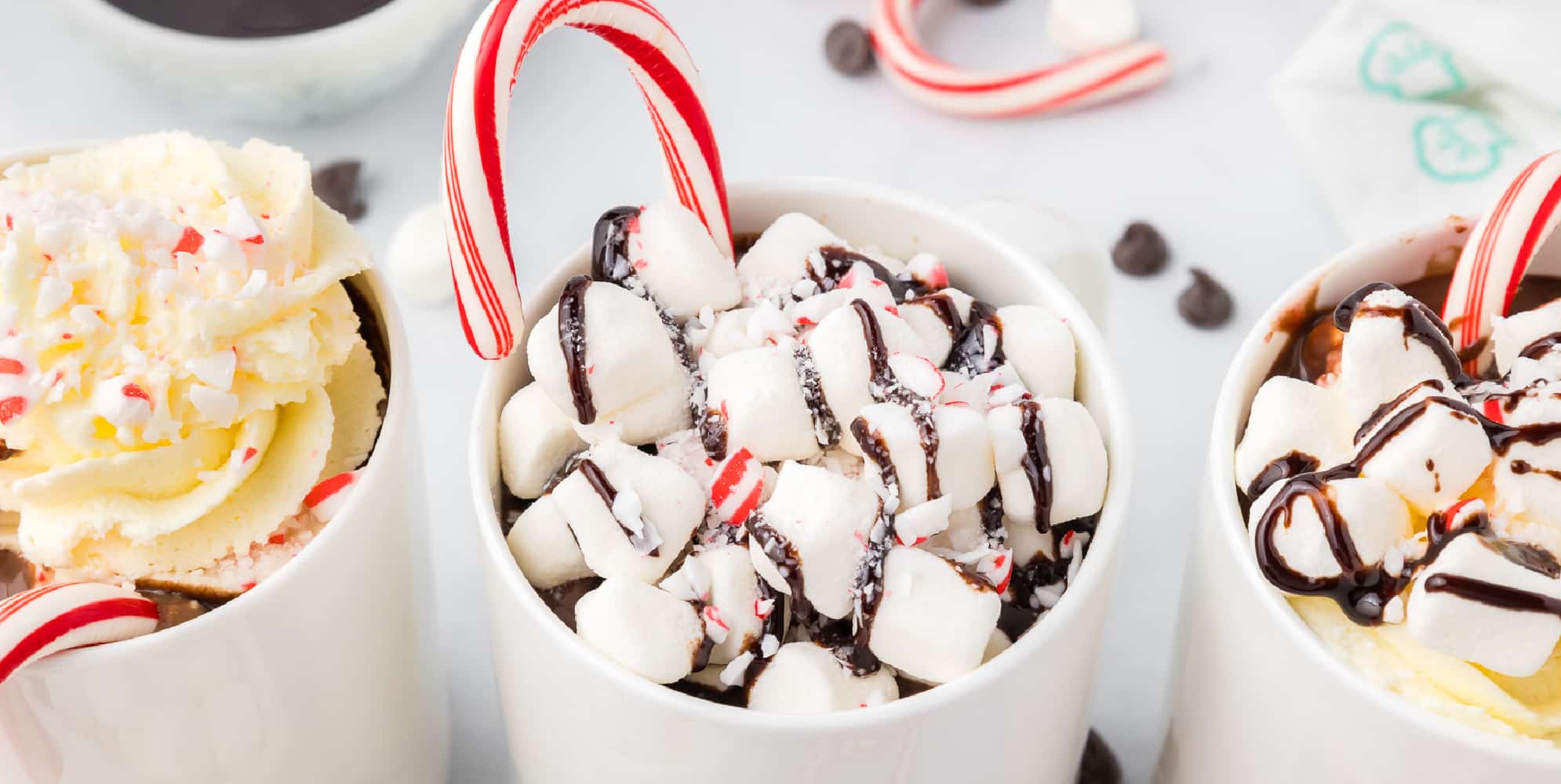 Three cups of hot chocolate with candy canes and marshmallows.