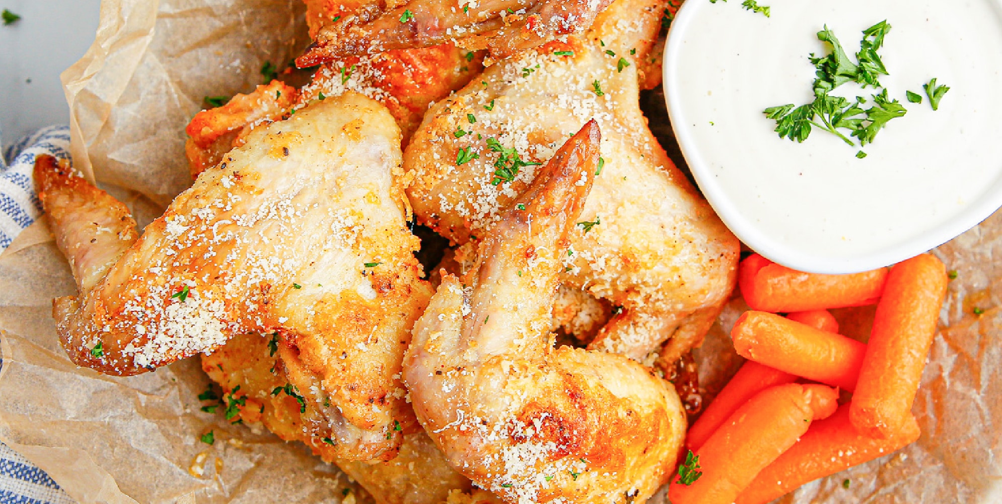 A plate of three chicken wings and carrots with a side of dipping sauce.