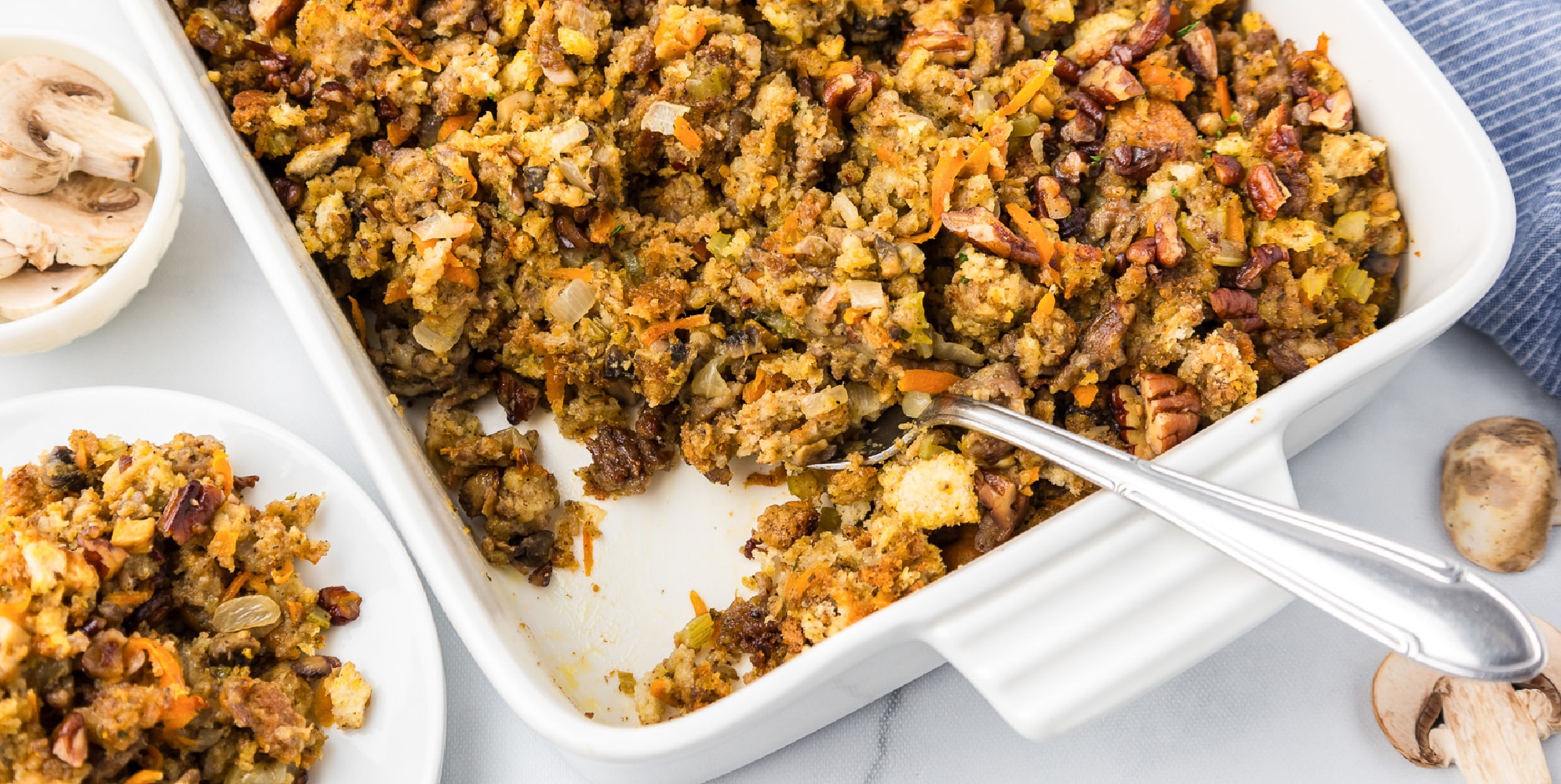 A wide view of casserole dish filled with stuffing and mushrooms with a scoop missing and a spoon.