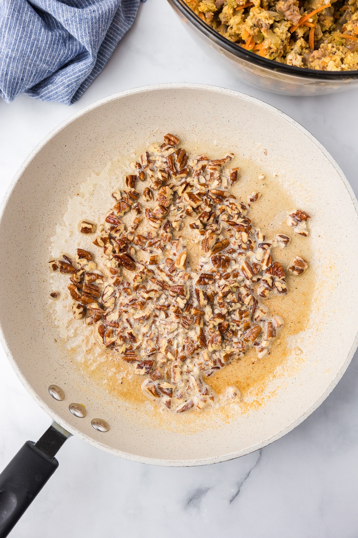 A frying pan with chopped pecans in melted butter.
