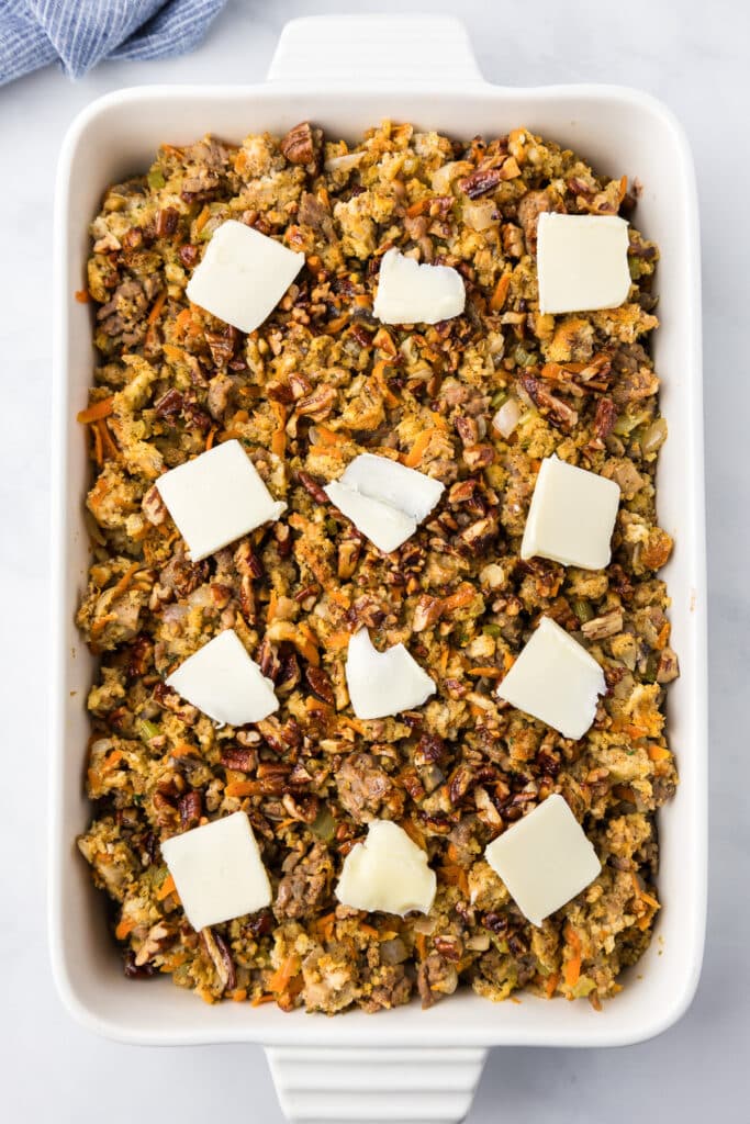 A rectangle baking dish filled with stuffing and pats of butter on top.