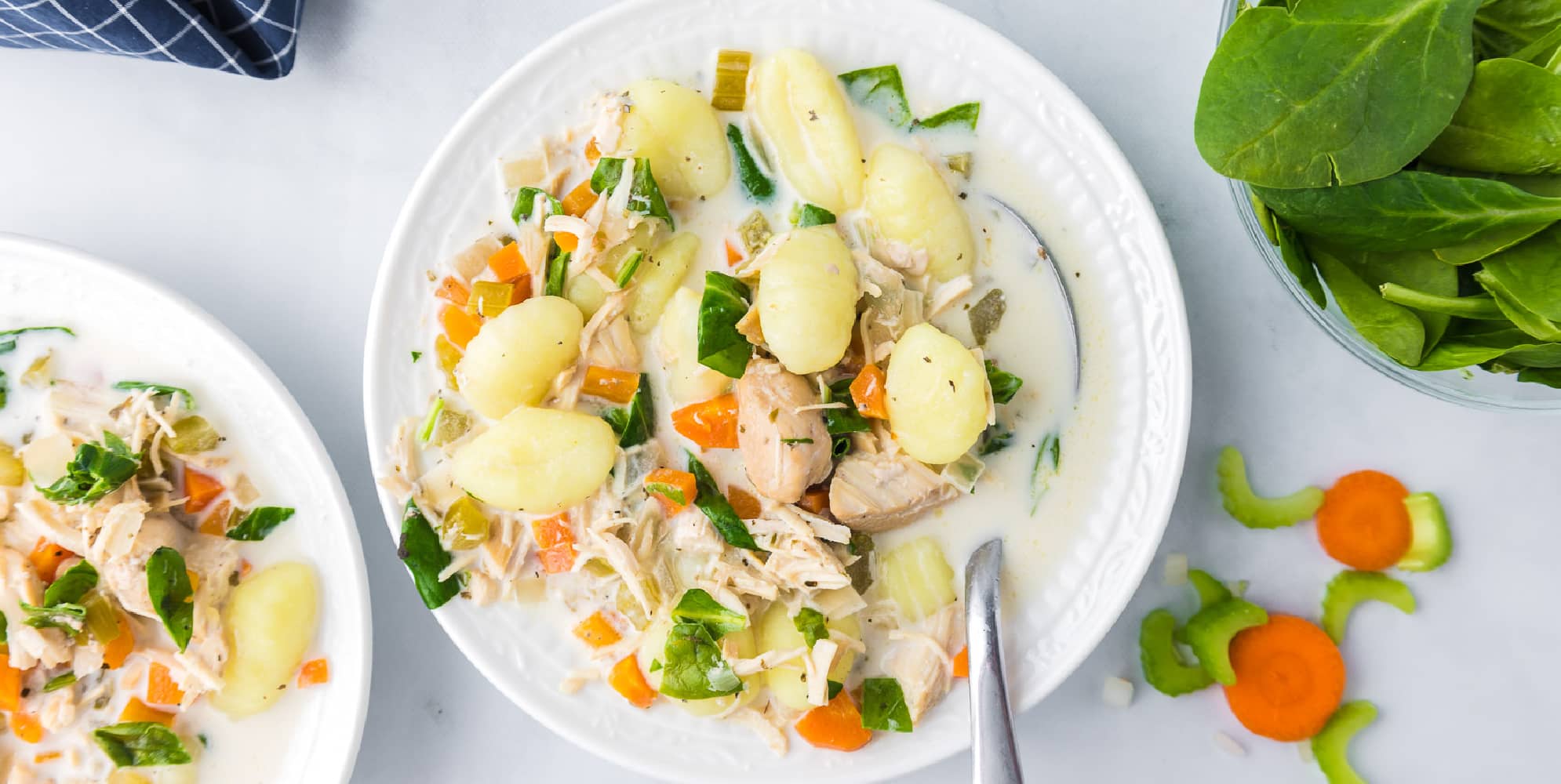 A bowl of creamy chicken gnocchi soup with vegetables in a bowl on a counter.