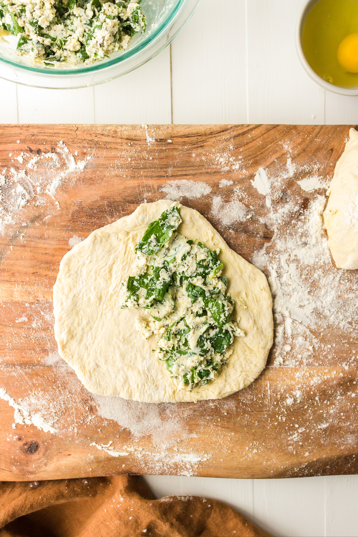 Spinach and ricotta mixture on half of a piece of pizza dough on a wooden cutting board.