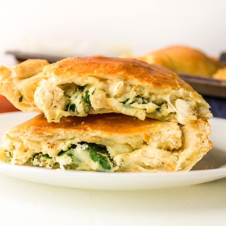 Cheesy chicken calzones stacked on a plate cut in half to see the filling inside.